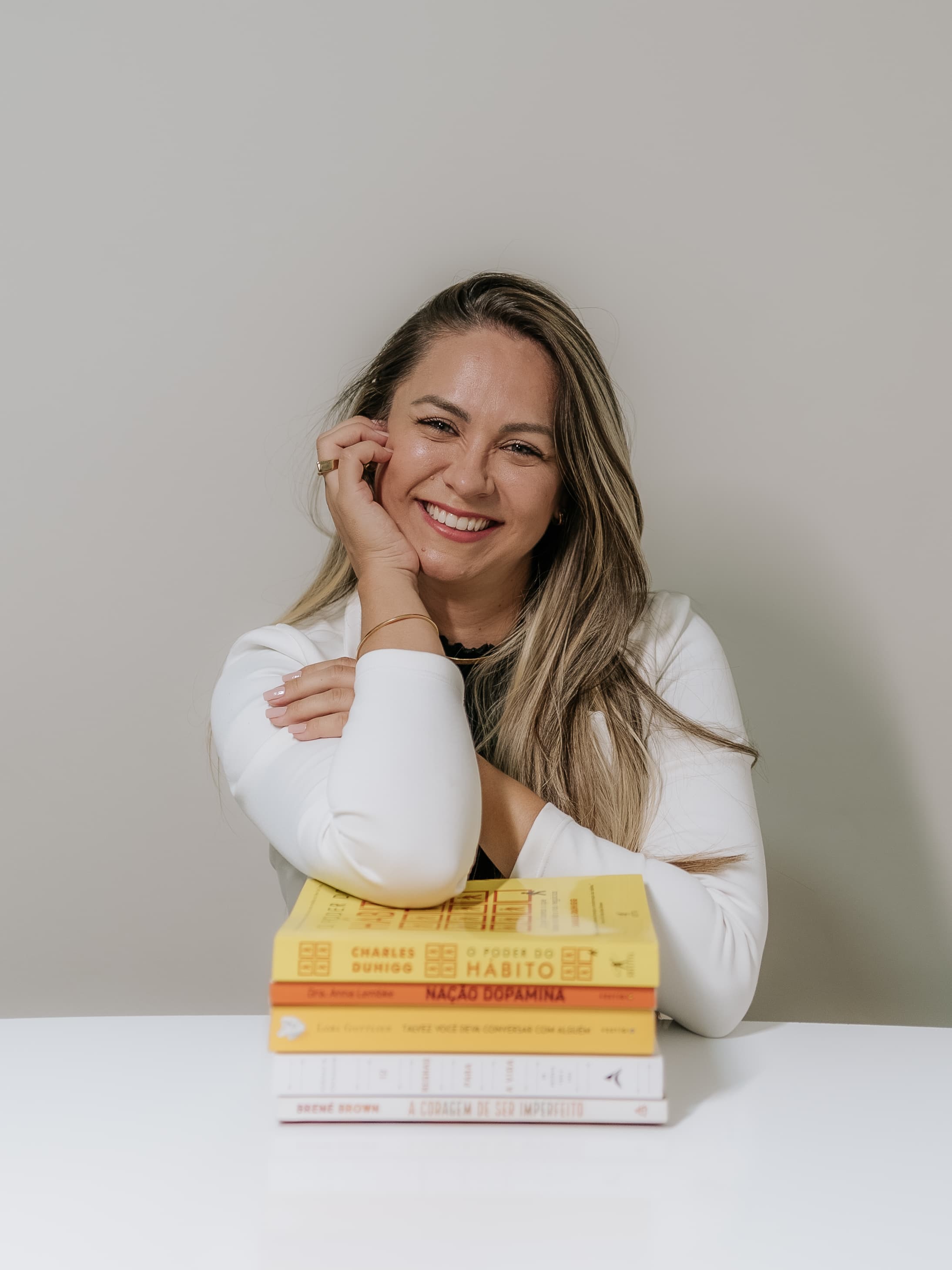 Cinthia Vallim apoiada em uma pilha de livros de psicologia